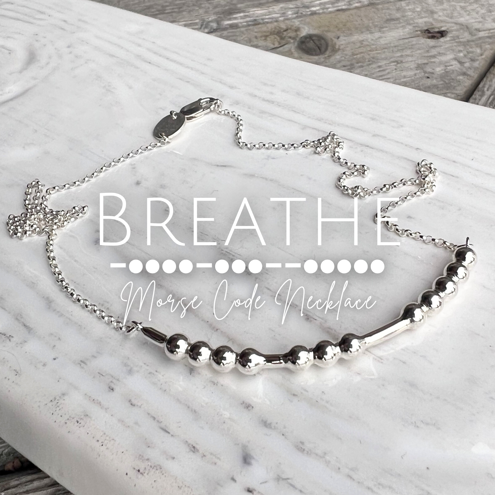 Silver Morse Code Necklace on a marble surface with 'BREATHE' text overlay