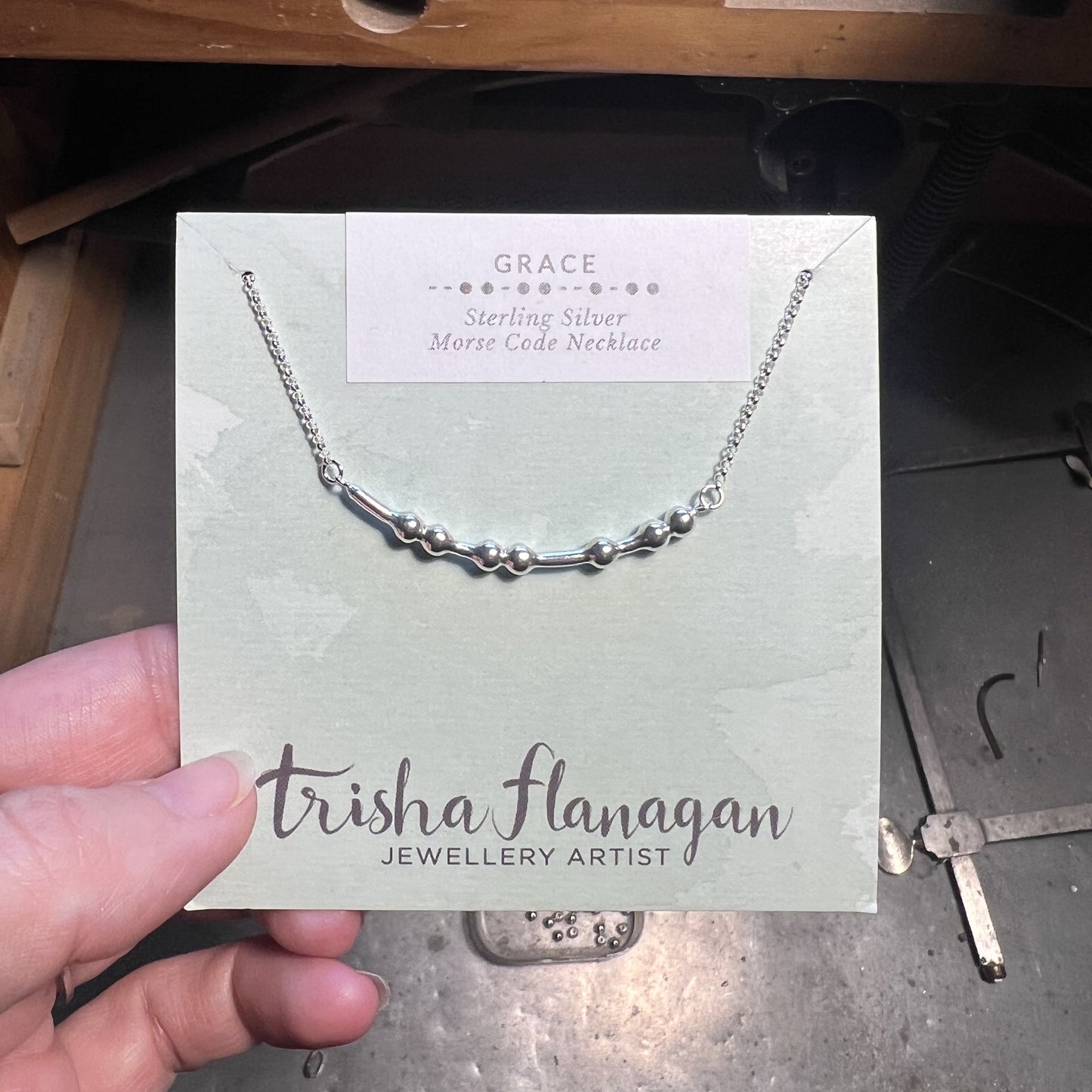 Silver Grace Morse Code Necklace on a Trisha Flanagan branded card held by a hand.