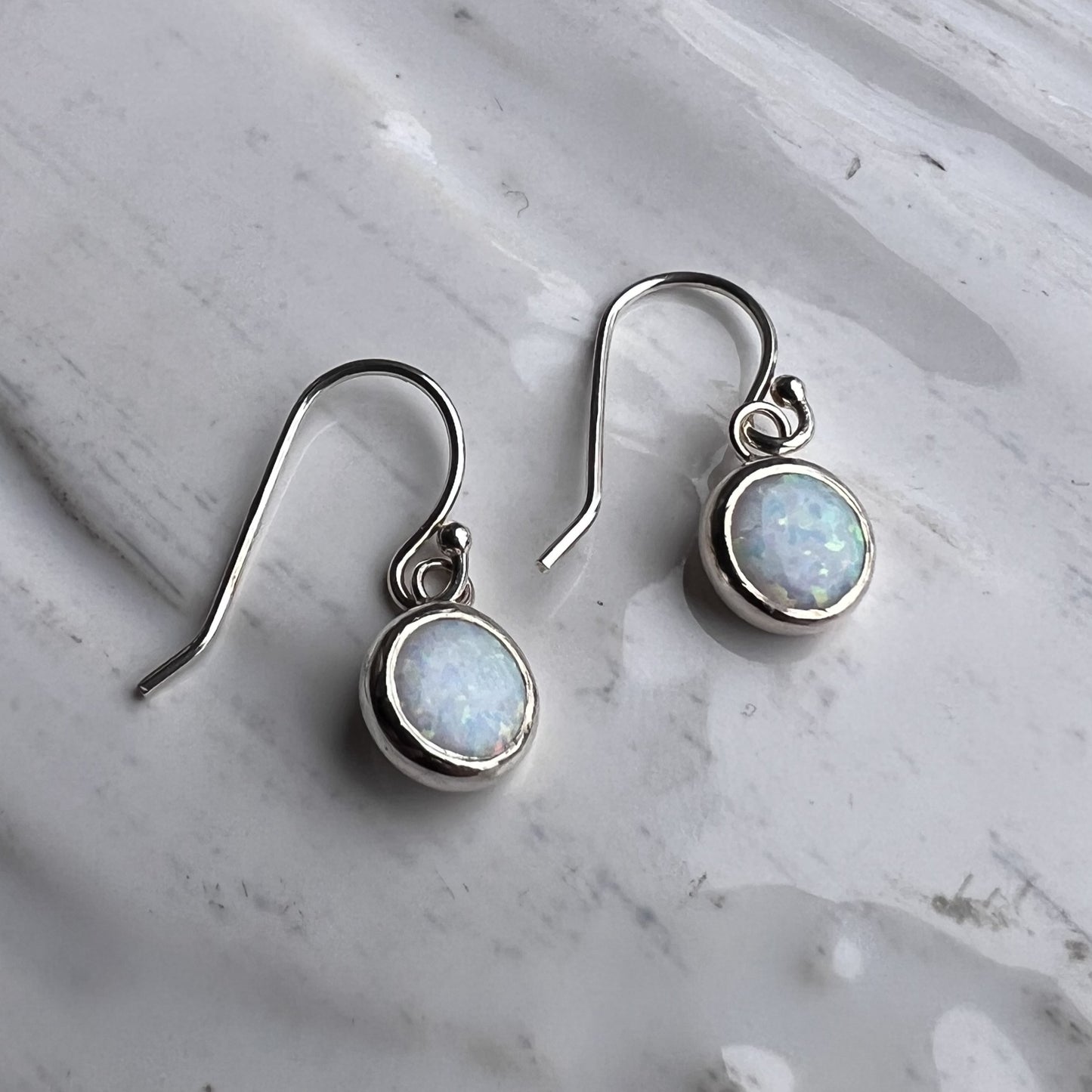 Silver earrings with round gemstones on a marble surface