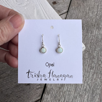 Opal earrings on a Trisha Flanagan Jewelry card held by a hand on a wooden surface.